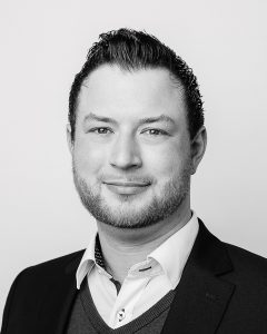 Hendrick Schieler, Mitarbeiter des Autohaus Rüd, lächelt in die Kamera – Porträtfoto im Innenbereich